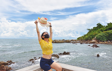 Young woman enjoying the beach under the sun wearing the protective face mask due to coronavirus.