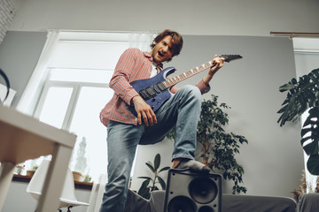 Young man plays guitar and sings a song at home with electric guitar
