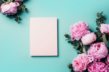 Feminine workspace with notebook, pink peony, eucalyptus flower on blue background. Top view, copy...