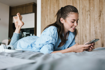 Photo of girl using mobile phone while lying on bed in living room