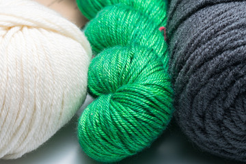Three skeins of different weight and color yarn.  Close up of cream, green and dark gray yarn.  Macro yarn.  Green yarn in the middle.