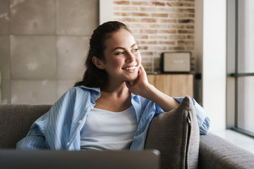 Photo of joyful nice girl using laptop while sitting on couch