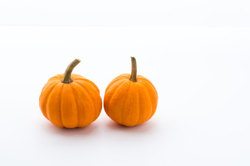 A pair of mini pumpkins next to each other on white surface with white background, with subtle gradients.  Small pumpkins for decoration up close.