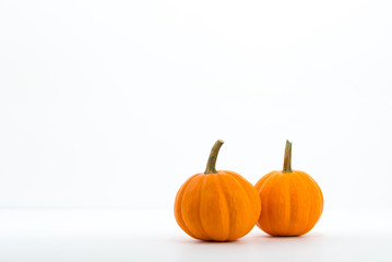 A pair of mini pumpkins next to each other on white surface with white background, with subtle gradients.  Small pumpkins for decoration up close.