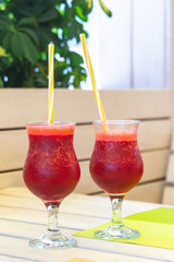 Berry smoothies in glass glasses. Summer refreshing drink. Two glasses with tubes on the blurred background of a summer cafe. Vitamin vegetarian cocktail.