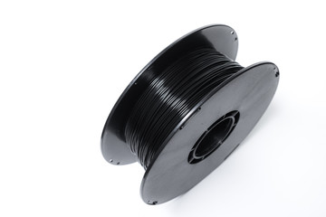 A spool of black 3d printer filament, up close.  Black PLA filament wound up on a spool, ready to...