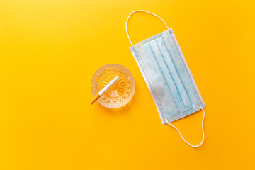Medical mask with cigarette and ashtray, isolated on yellow background.