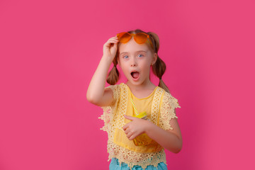 a little girl in sunglasses with a cocktail on a pink background
