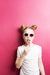 Bright colors: a girl with a striped lollipop and sunglasses on a bright pink background.