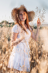 Ginger girl with freckles in the wheat field wearing a summer hat.