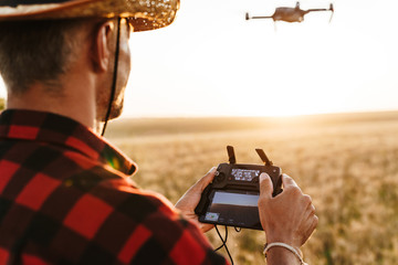 Image from back of man using drone while standing at cereal field