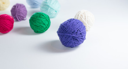 Colorful yarn balls spread around a white surface, with extra space for copy.  Purple yarn in front, with other colors behind.  Knitting or crochet materials ready to made into a garment.