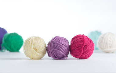 Three small balls of yarn in a row on a light surface, with other colored balls of yarn in the background.  Knitting or crochet materials up close with side light.