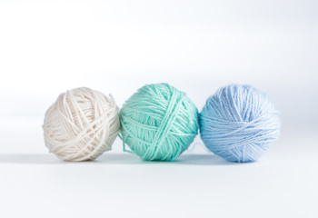 Three balls of yarn lined up on a white surface and white background.  Up close view of cream, mint, and light blue colored yarn balls with space for copy above.