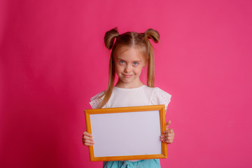 Portrait of a girl holding an empty frame, upset place for text Studio on a pink background