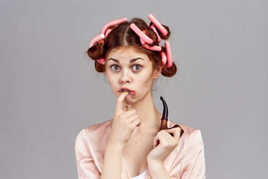 woman with curlers on her head in a dressing gown housewife smoking pipe in hand gray background