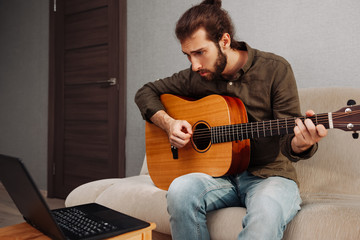 Concentrated man learning to play acoustic guitar at home by video tutorial
