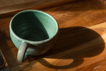 A large teal coffee mug sits on a wooden serving tray in the early morning sun.  An empty coffee mug with extra room for copy on the right.
