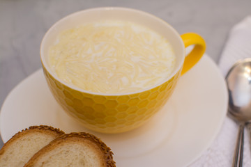 Milk noodle soup in a yellow ceramic bowl and two slices of white bread with sesame seeds on a gray table.