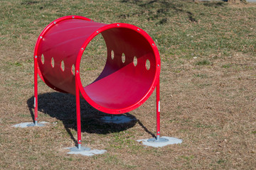 A large red tube made for dog agility courses.  The dog runs and jumps through the tube, which is anchored to the ground.