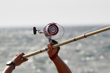 Primer plano de pescador con su caña de carrete pescando en el mar.