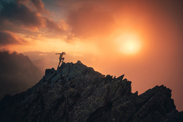 Sport photo in mountains. Silhouette of runner on the top of the hill, orange sunset sky in background. Edit space.