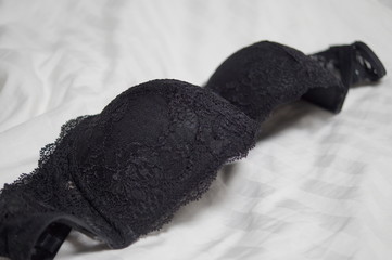 A black bra is lying on a white bed