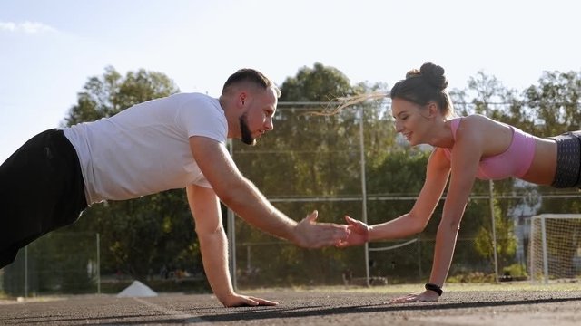Close-up of a guy and a girl training in the summer at the stadium, they stand in support lying on their hands and clap each other on the hands.