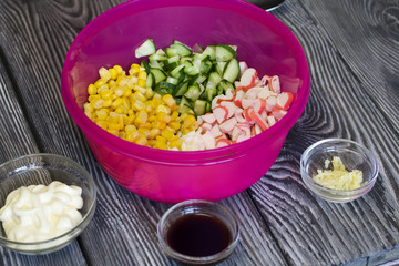 Crushed crab sticks, boiled chicken eggs, cucumber and corn. In the container to prepare the salad. Next to mayonnaise, garlic and soy sauce. On painted pine boards.