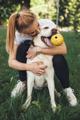 Close up photo of a blonde girl and her golden retriever playing with a ball on the grass