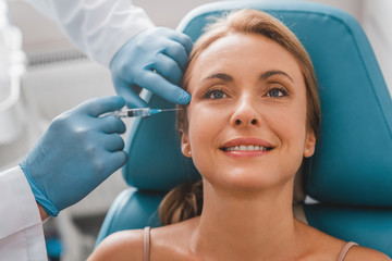 Attractive adult woman getting rejuvenating facial injections in clinic