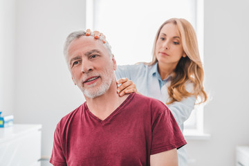 Female orthopedist examining senior patient's neck in clinic