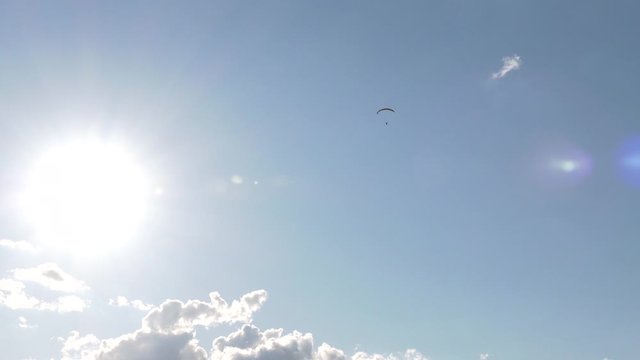 Paraglider flying over fields in sunny day. Paraglider in the blue sky.  High altitude. The athlete turns the thermal current. Rise up. Weather for flights. Satisfaction.  

