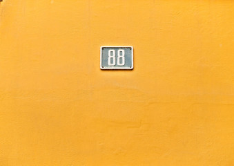 Number 88, eighty-eight, small blue plate on warm yellow wall.