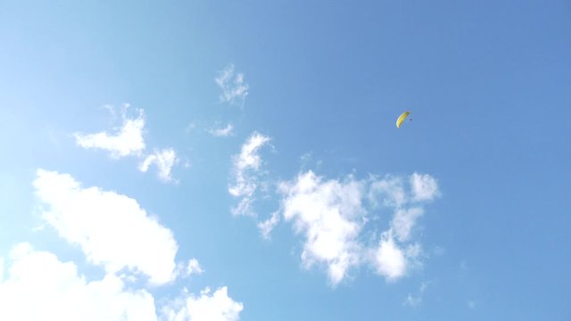 Paraglider flying over fields in sunny day. Paraglider in the blue sky.  Silhouette of paraglide flying in the sky with clouds in a light of sunrise. Paraglider flying in the air stream.
