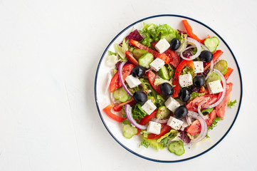 Vegetable salad with olives and feta cheese. Greek salad in a plate on a white concrete background. Copy space.