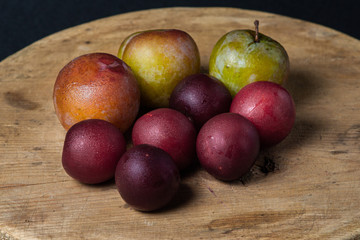 Plums on a black background. Plums of two varieties lie on a wooden surface. Summer harvest