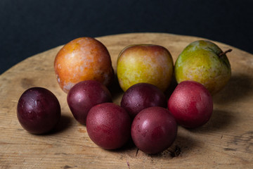 Plums on a black background. Plums of two varieties lie on a wooden surface. Summer harvest