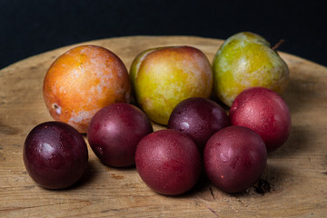 Plums on a black background. Plums of two varieties lie on a wooden surface. Summer harvest