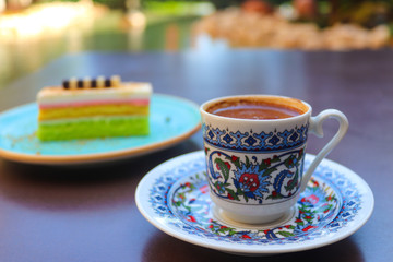 Traditional turkish coffee in a coffee cup with a traditional pattern with colorful cake on the terrace in restaurant. Close-up, selective focus