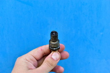 Dirty car spark plug in hand on blue background