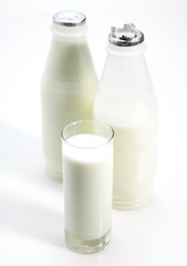 Glass and Bottles of Milk against White Background