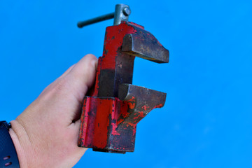 Small iron vise in hand on a blue background