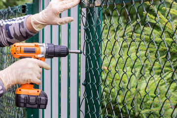 Work with a drill-screwdriver with an electric battery to strengthen the mesh on a metal fence.