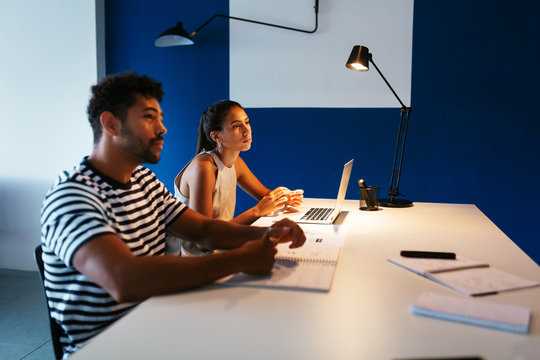 Pensive couple sitting at table with laptop and notebook