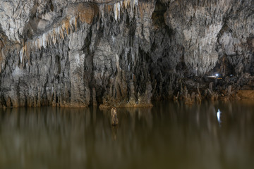 Grey rock stalactite wall and water in the cave