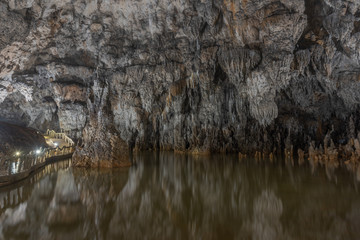 Grey rock stalactite wall and water in the cave