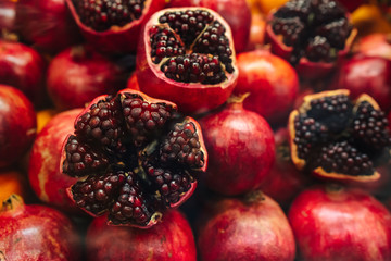 Juicy and ripe pomegranate with peel taken off, exposing fresh seeds, laying on pile of pomegranates