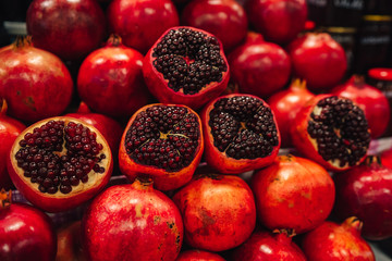 Juicy and ripe pomegranate with peel taken off, exposing fresh seeds, laying on pile of pomegranates
