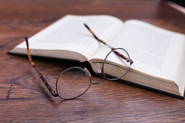 Pair of glasses with a book on wood surface